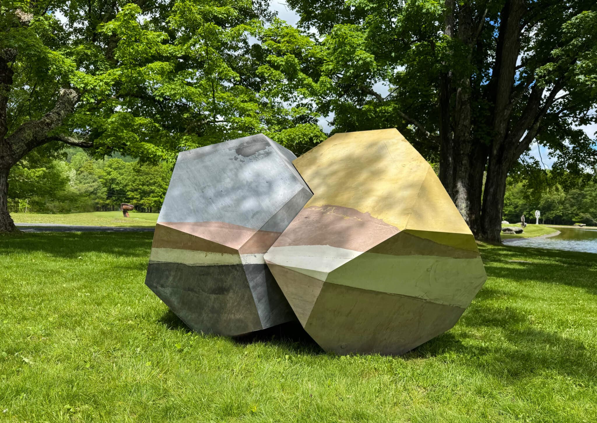 An angular concrete sculpture is surrounded by trees in a grassy area.
