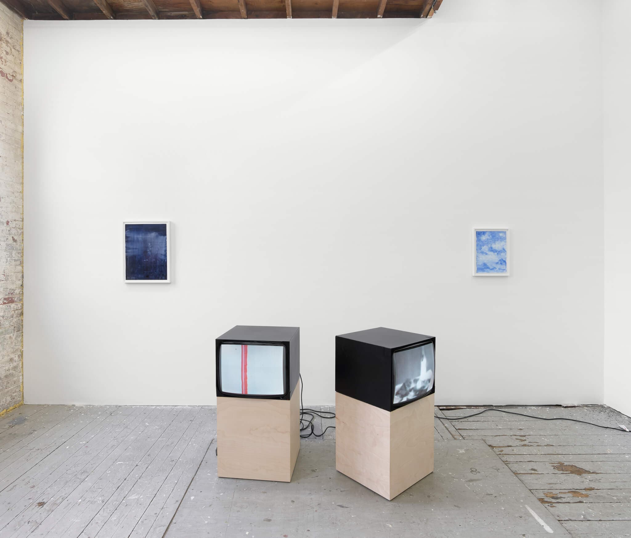 Two CRT monitors rest on pedestals in the center of a gallery, flanked on either side by blue watercolor works.